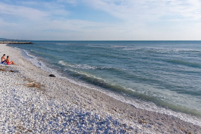 Marina di Pisa, spiaggia di ciottoli con mare calmo e due bagnanti; ideale per famiglie