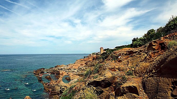 Spiaggia di Calafuria con scogli, torre del Romito e bagnanti nel mare turchese