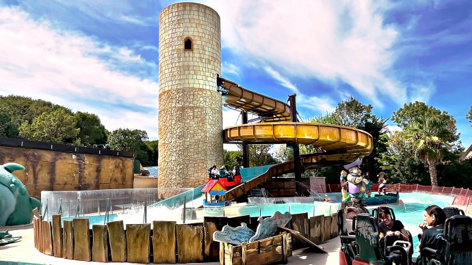 Attrazione acquatica con scivolo e torre in pietra al Cavallino Matto, Toscana; persone in gommone