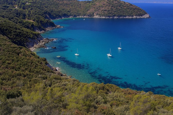 Cala Grande all’Argentario con mare turchese, scogliere e barche a vela ancorate