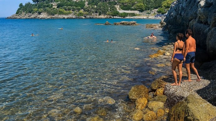 Spiaggetta Pozzarello a Porto Santo Stefano, coppia su scogli osserva mare trasparente e bagnanti
