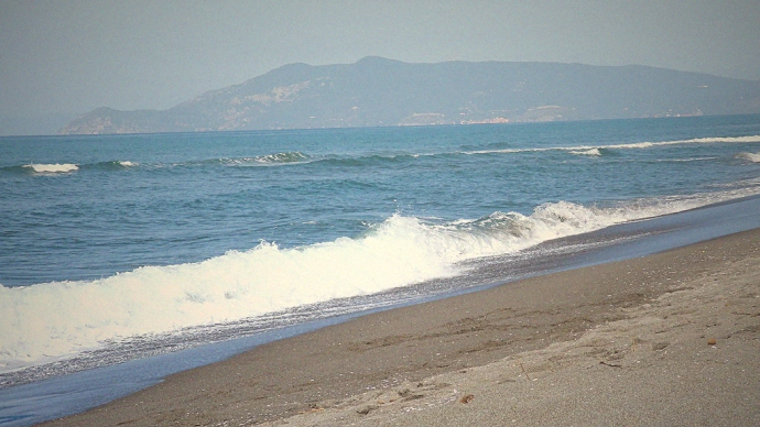 Onde sulla Spiaggia di Chiarone con vista su Monte Argentario, litorale sabbioso in Maremma.