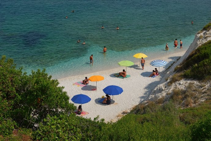 Capo Bianco all’Elba: spiaggia di ciottoli bianchi, mare turchese e ombrelloni colorati.