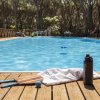 Una piscina contornata da alberi, con racchette, una pallina e un asciugamano su un ponte in legno.