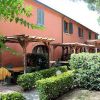 Edificio arancione con pergolati in legno e tavoli all'aperto, circondato da siepi verdi.