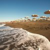 Spiaggia con ombrelloni gialli, sabbia bagnata dalle onde e cielo limpido.