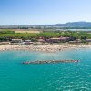 Spiaggia affollata con ombrelloni, mare e colline sullo sfondo.