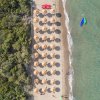 Vista dall'alto di ombrelloni su una spiaggia accanto a una linea di alberi e mare con canoe.