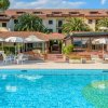 Piscina con lettini e ombrelloni davanti a un edificio con tetti rossi e palme.