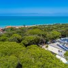 Vista aerea di pineta costiera con mare azzurro e edificio con pannelli solari.