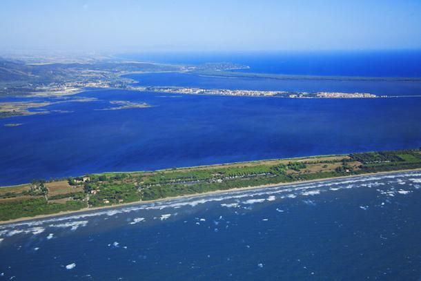 Vista aerea di una costa con mare blu e spiaggia in primo piano.