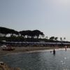 Spiaggia con ombrelloni blu, poche persone in acqua, linee di alberi sullo sfondo.
