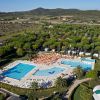 Vista aerea di un grande complesso con due piscine, ombrelloni arancioni e vegetazione rigogliosa.