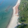 Vista aerea di una spiaggia con lettini e ombrelloni, affiancata da una foresta verde.